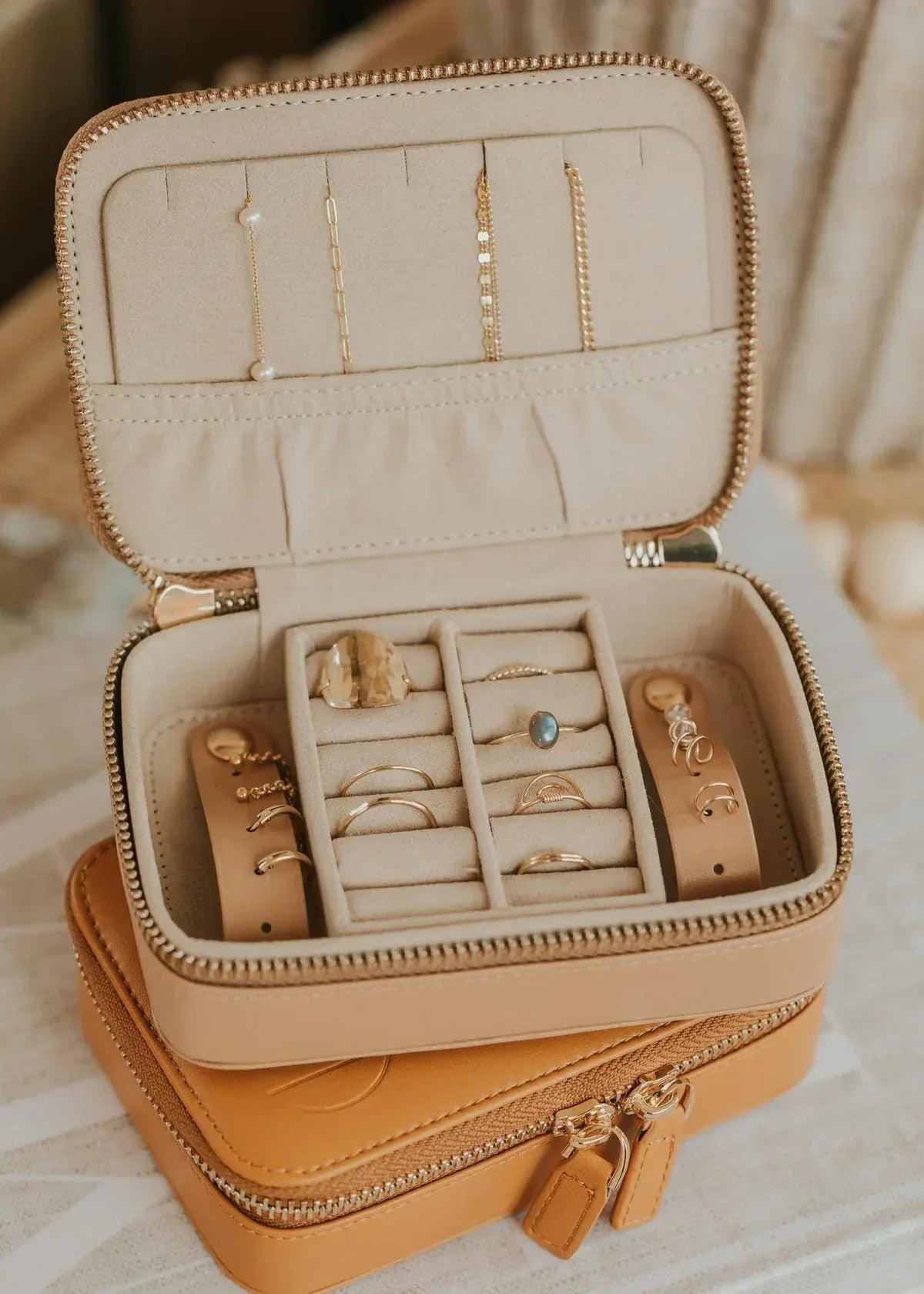 Beige zippered jewelry organizer with rings, necklaces, and bracelets neatly stored inside